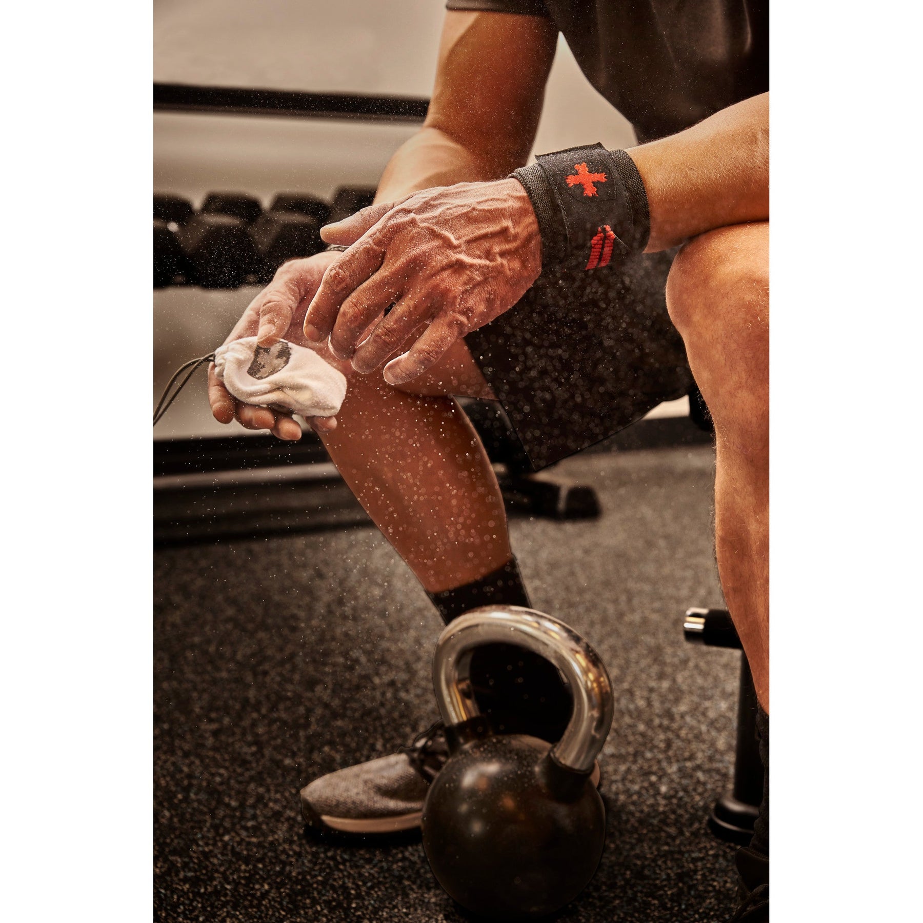Hands squeezing Harbinger chalk ball with dust cloud, kettlebell on gym floor