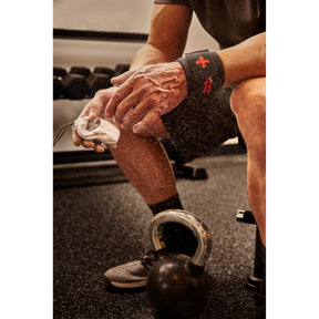 Hands squeezing Harbinger chalk ball with dust cloud, kettlebell on gym floor
